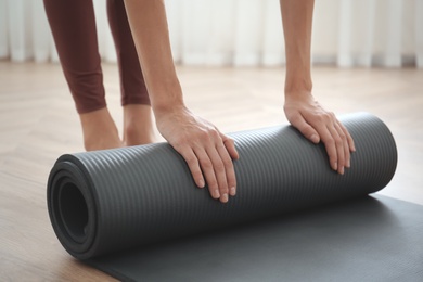 Woman rolling grey yoga mat indoors, closeup