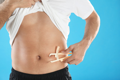 Man measuring body fat layer with caliper on light blue background, closeup. Nutritionist's tool