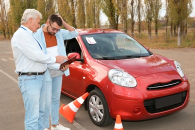 Senior instructor and man near car outdoors. Passing driving license exam