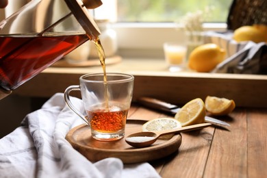 Photo of Pouring delicious tea into glass cup at wooden table, closeup. Space for text
