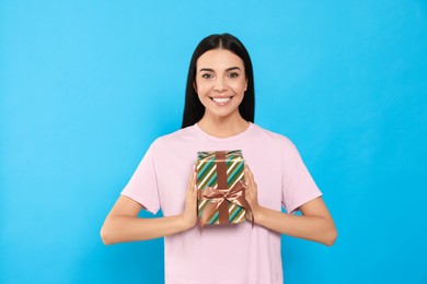 Happy young woman holding gift box on light blue background