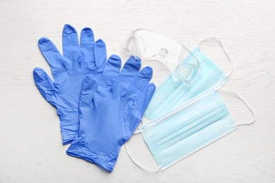 Medical gloves, masks and goggles on white wooden background, flat lay