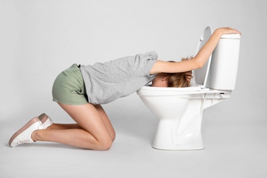 Young woman vomiting in toilet bowl on gray background