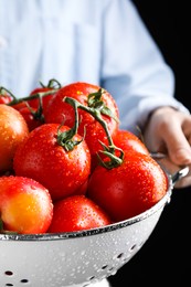 Woman holding colander with fresh ripe tomatoes on black background, closeup