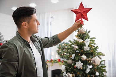 Photo of Man decorating Christmas tree with star topper indoors