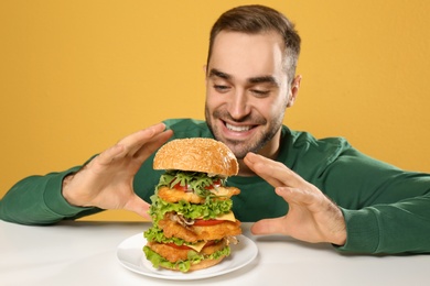 Young hungry man eating huge burger at table