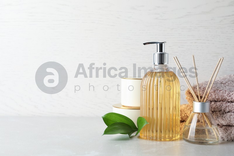 Photo of Stylish soap dispenser, air freshener, towels and leaves on light table. Space for text