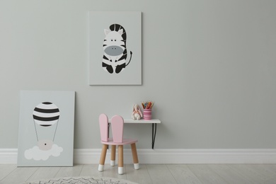 Photo of Stylish child's room interior with adorable paintings, small table and chair. Space for text