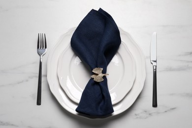 Plate with dark blue fabric napkin, decorative ring and cutlery on white marble table, flat lay