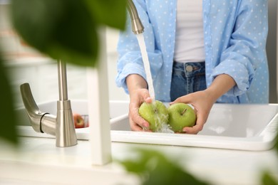 Photo of Woman washing fresh green apples in kitchen sink, closeup