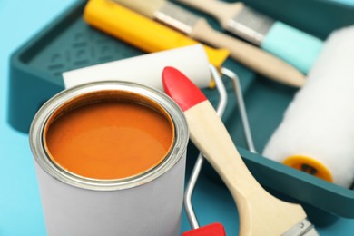 Photo of Can of orange paint, brushes, rollers and container on turquoise background, closeup