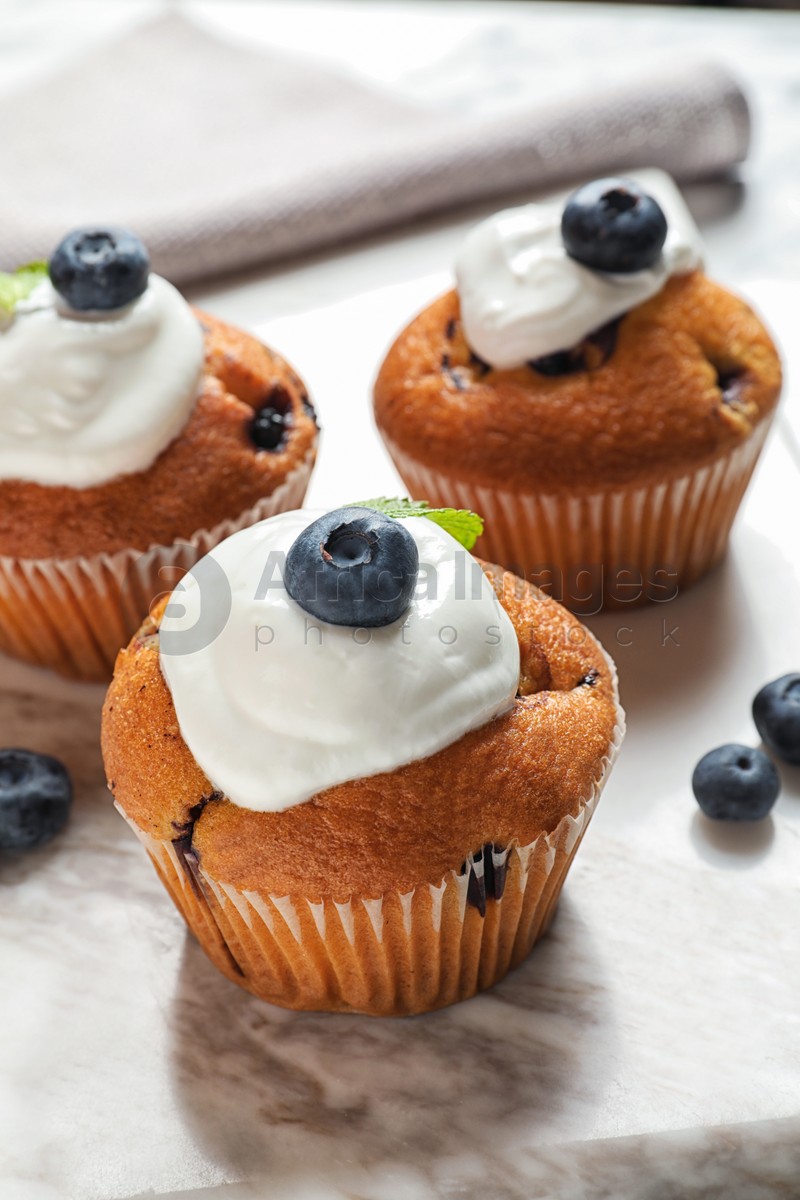 Photo of Marble board with tasty muffins, cream and blueberries on table