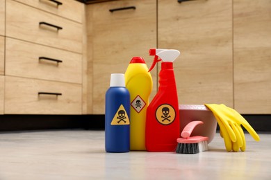 Bottles of toxic household chemicals with warning signs, gloves and brush on floor indoors, space for text