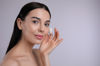 Woman using silkworm cocoon in skin care routine on light grey background. Space for text