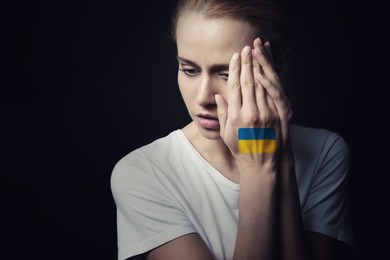 Upset young woman with picture of Ukrainian flag on hand against black background. Stop war in Ukraine