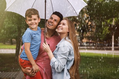Happy family with umbrella walking under rain in park
