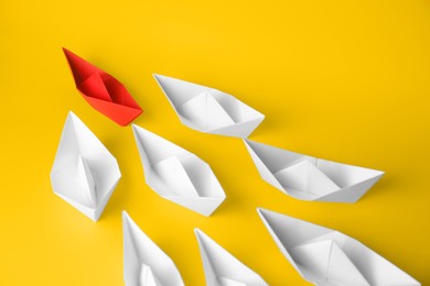 Photo of Group of paper boats following red one on yellow background. Leadership concept