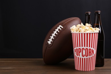 American football ball with popcorn and beer on wooden table. Space for text