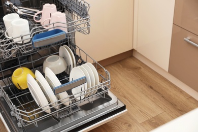 Photo of Open dishwasher with clean tableware in kitchen. Space for text