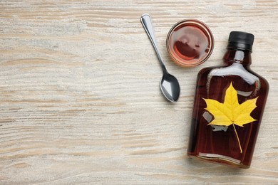 Tasty maple syrup and dry leaf on wooden table, flat lay. Space for text