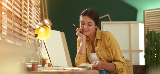 Young woman drawing on paper at table indoors. Banner design