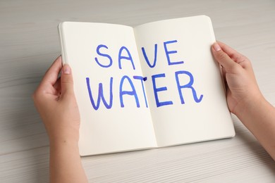 Woman holding notebook with words Save Water on wooden background, closeup