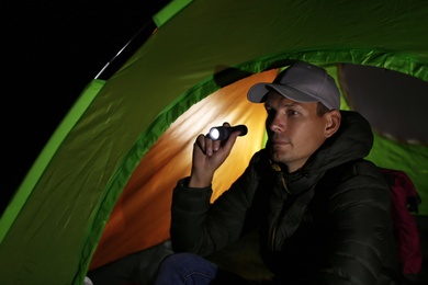 Man with flashlight sitting in tent at night
