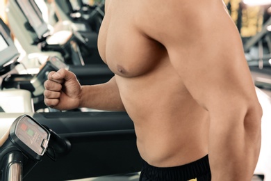 Strong young man on treadmill in gym, closeup of torso