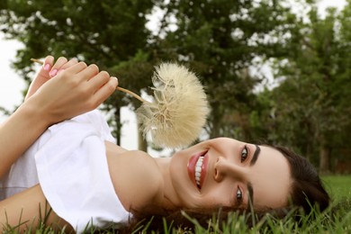 Beautiful young woman with large dandelion lying on green grass in park. Allergy free concept