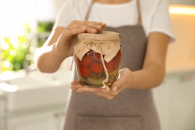 Woman holding jar of pickled tomatoes indoors, closeup