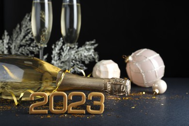 Happy New Year 2023! Bottle of sparkling wine and festive decor on table against black background