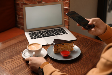 Male blogger taking photo of dessert and coffee at table in cafe, closeup