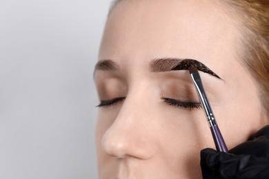 Beautician applying tint during eyebrows correction procedure on light grey background, closeup