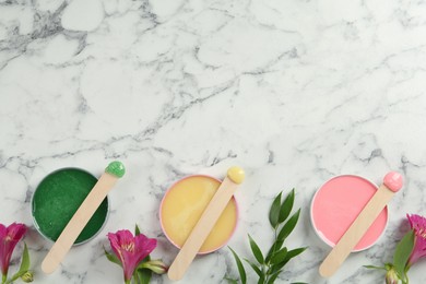 Spatula with different types of wax and flowers on white marble table, flat lay. Space for text