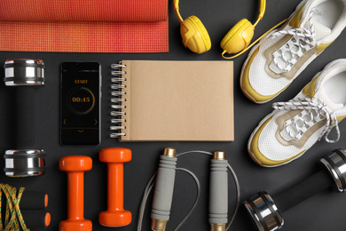 Photo of Flat lay composition with fitness equipment, notebook  and smartphone on dark background, space for text