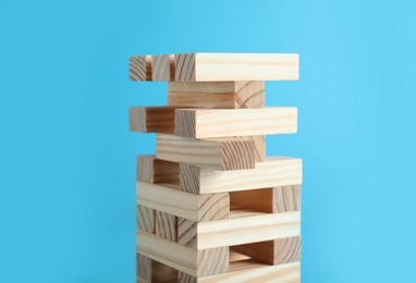 Jenga tower made of wooden blocks on light blue background, closeup
