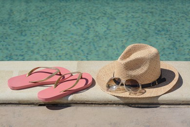 Stylish hat, flip flops and sunglasses near outdoor swimming pool on sunny day. Beach accessories