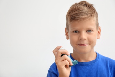 Photo of Little boy with asthma inhaler on light background