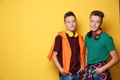 Teenage twin brothers with headphones on color background. Space for text