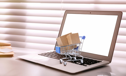 Online shopping. Small cart with boxes on laptop indoors