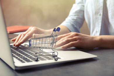Woman shopping online using laptop, focus on small cart