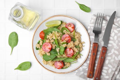 Photo of Delicious quinoa salad with tomatoes and spinach leaves served on white tiled table, flat lay