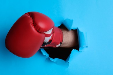 Man breaking through light blue paper with boxing glove, closeup