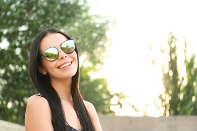 Beautiful young woman wearing stylish sunglasses outdoors. Space for text