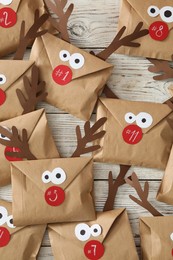 Photo of Set of gifts in envelopes with deer faces on white wooden table, flat lay. Christmas advent calendar