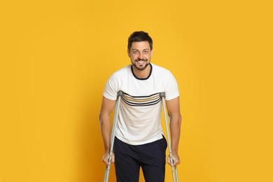 Portrait of happy man with crutches on yellow background