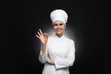 Photo of Happy female chef with wooden spoon showing ok gesture on black background