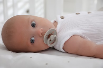 Cute little baby with pacifier lying on bed, closeup