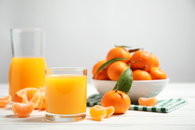 Photo of Glass of fresh tangerine juice and fruits on white wooden table