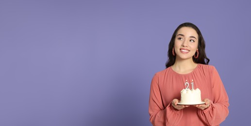 Photo of Coming of age party - 21st birthday. Smiling woman holding delicious cake with number shaped candles on violet background